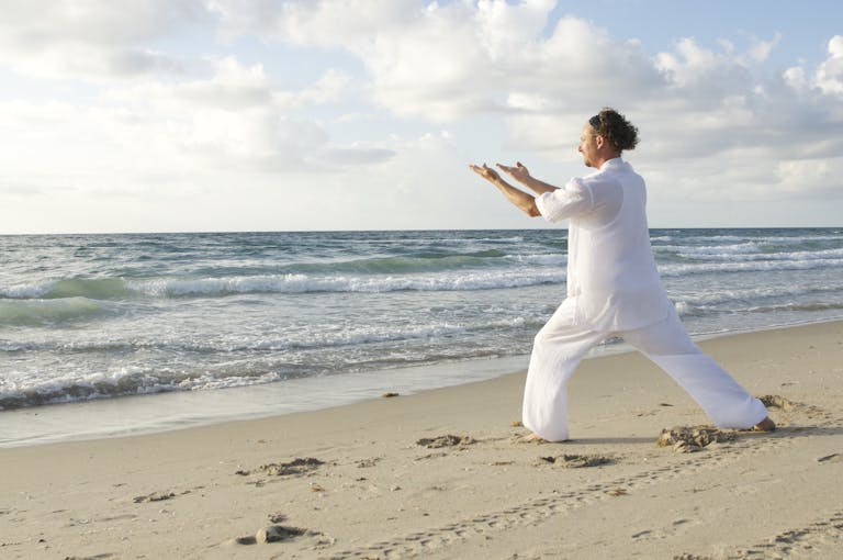 A serene scene of a man practicing Tai Chi on a quiet beach with gentle waves.